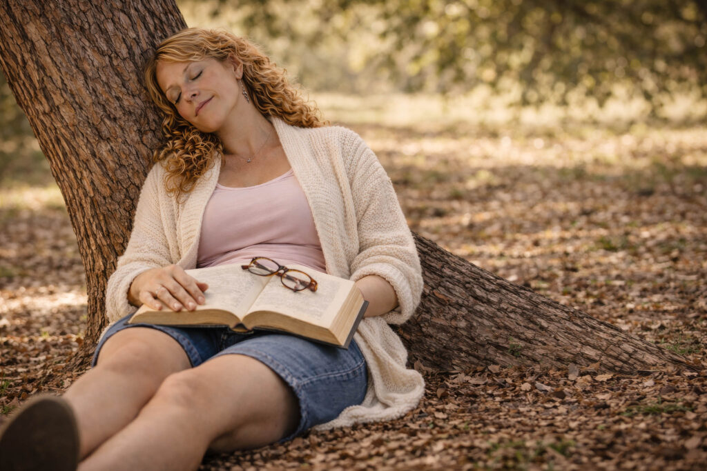 June Haunsby resting under a tree with a book on her lap, eyes closed
