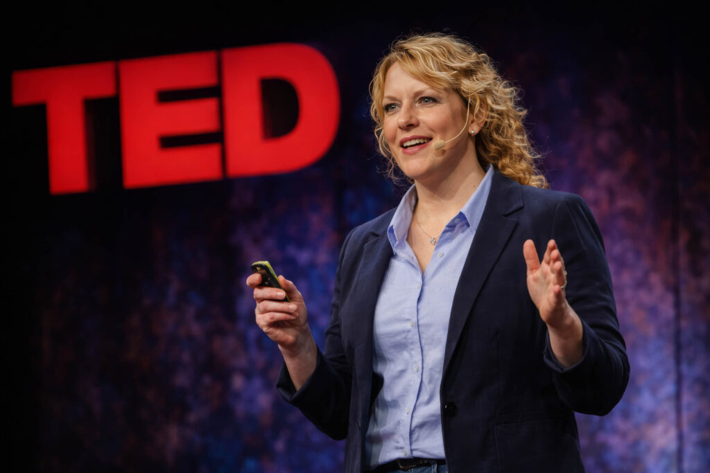 June Haunsby speaking on stage with a headset microphone during a public talk