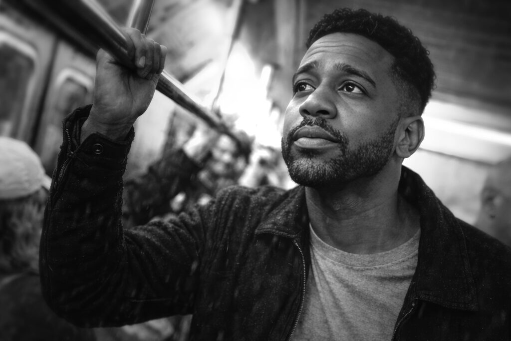 Black and white portrait of Luca Haunsby standing in a subway train, looking thoughtful