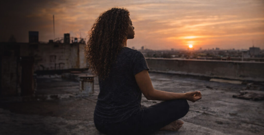 Zaya Haunsby sitting in meditation on a rooftop while watching the sunset